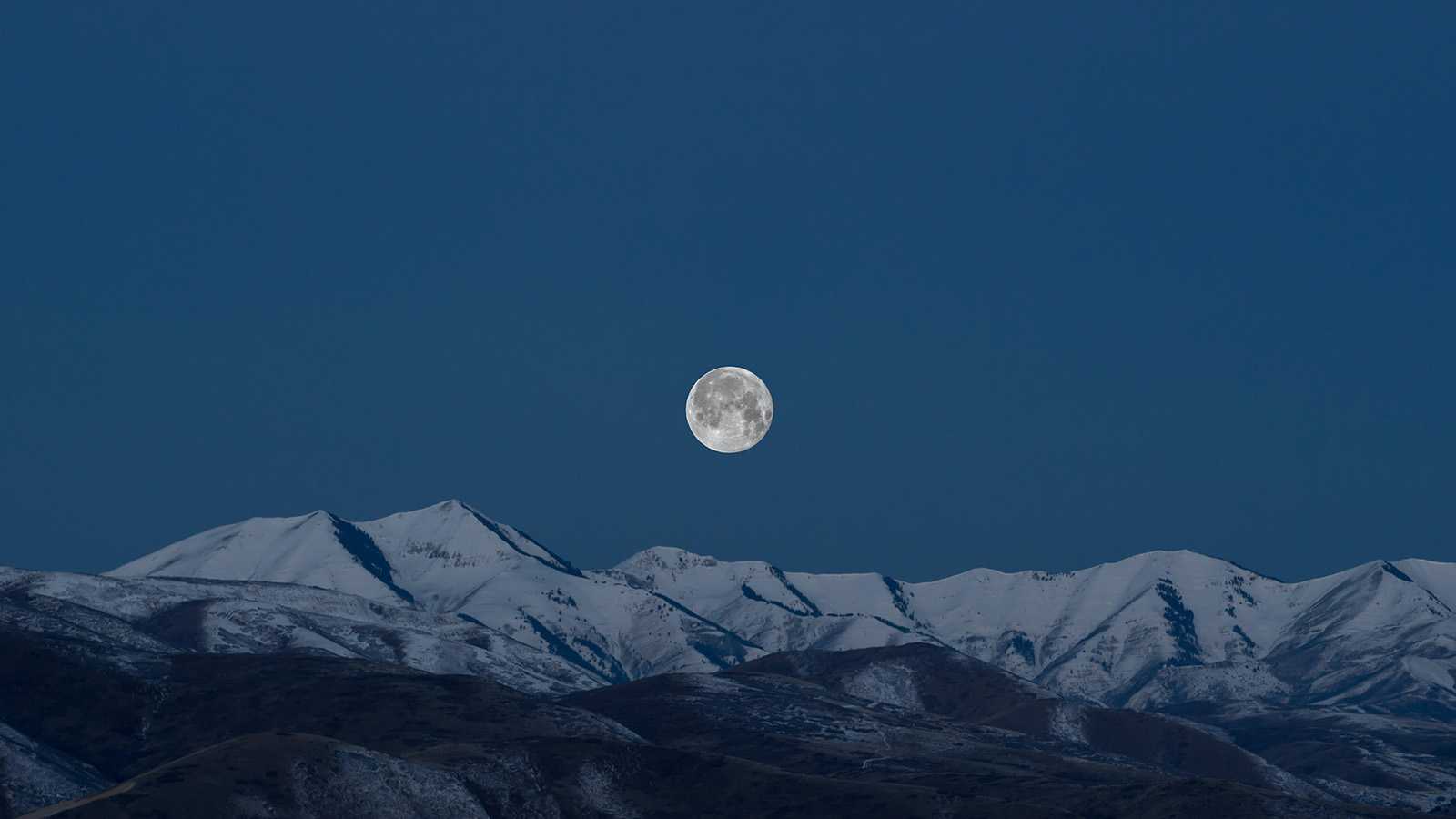 A full moon above snow-capped mountains
