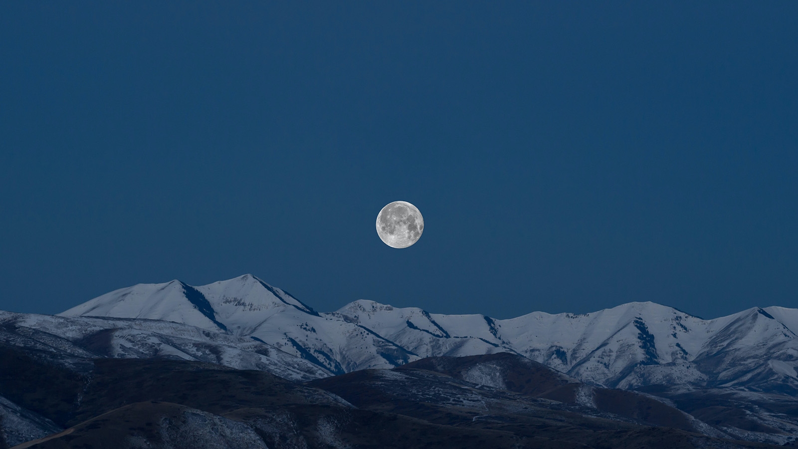 A full moon above snow-capped mountains